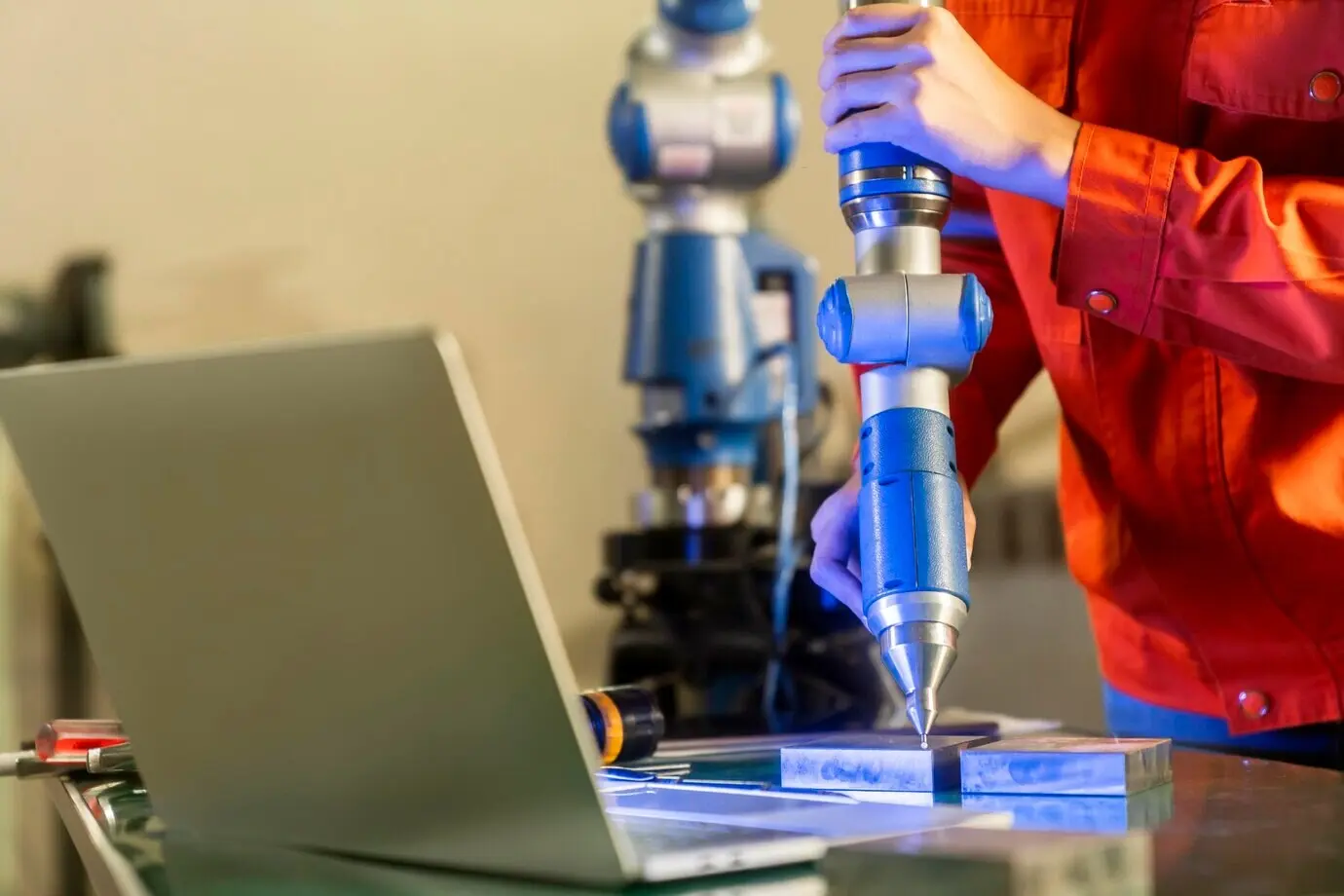 Asian female engineering specialist with a manipulator-arm measuring machine, performing three-dimensional coordinate measurements and 3D size checks of parts using a CMM after the machining process.